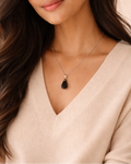 Woman wearing a necklace with a black pendant against a neutral background