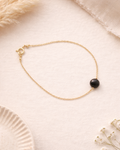 Gold bracelet with a black bead on a soft beige background