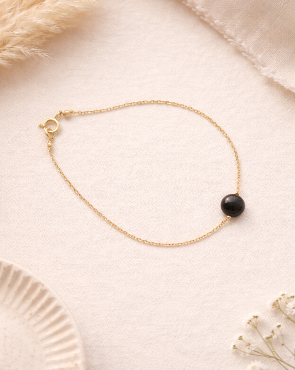 Gold bracelet with a black bead on a soft beige background