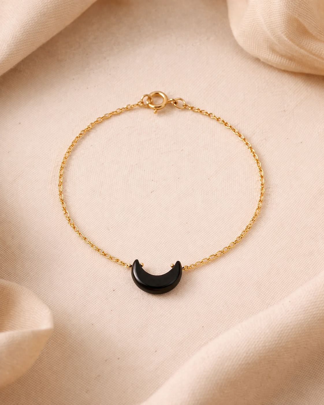 Gold bracelet with a black crescent moon charm on a beige fabric background