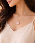 Woman wearing a delicate necklace with a pink pendant against a neutral background