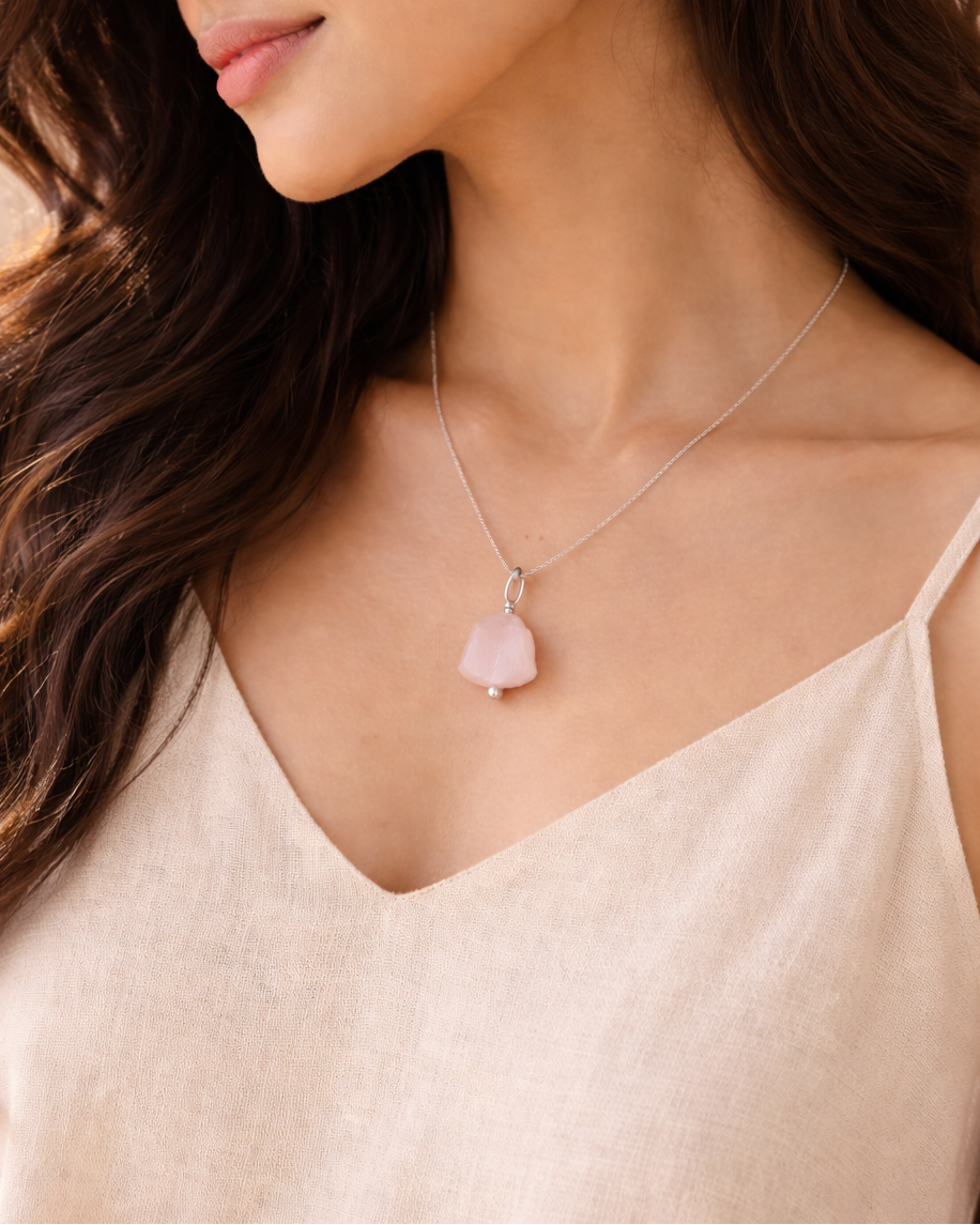 Woman wearing a delicate necklace with a pink pendant against a neutral background