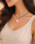Woman wearing a necklace with a pink pendant against a neutral background