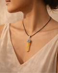 Woman wearing a necklace with a yellow pendant against a neutral background