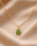 Gold necklace with a green pendant on a beige fabric background
