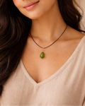 Woman wearing a necklace with a green pendant against a beige background