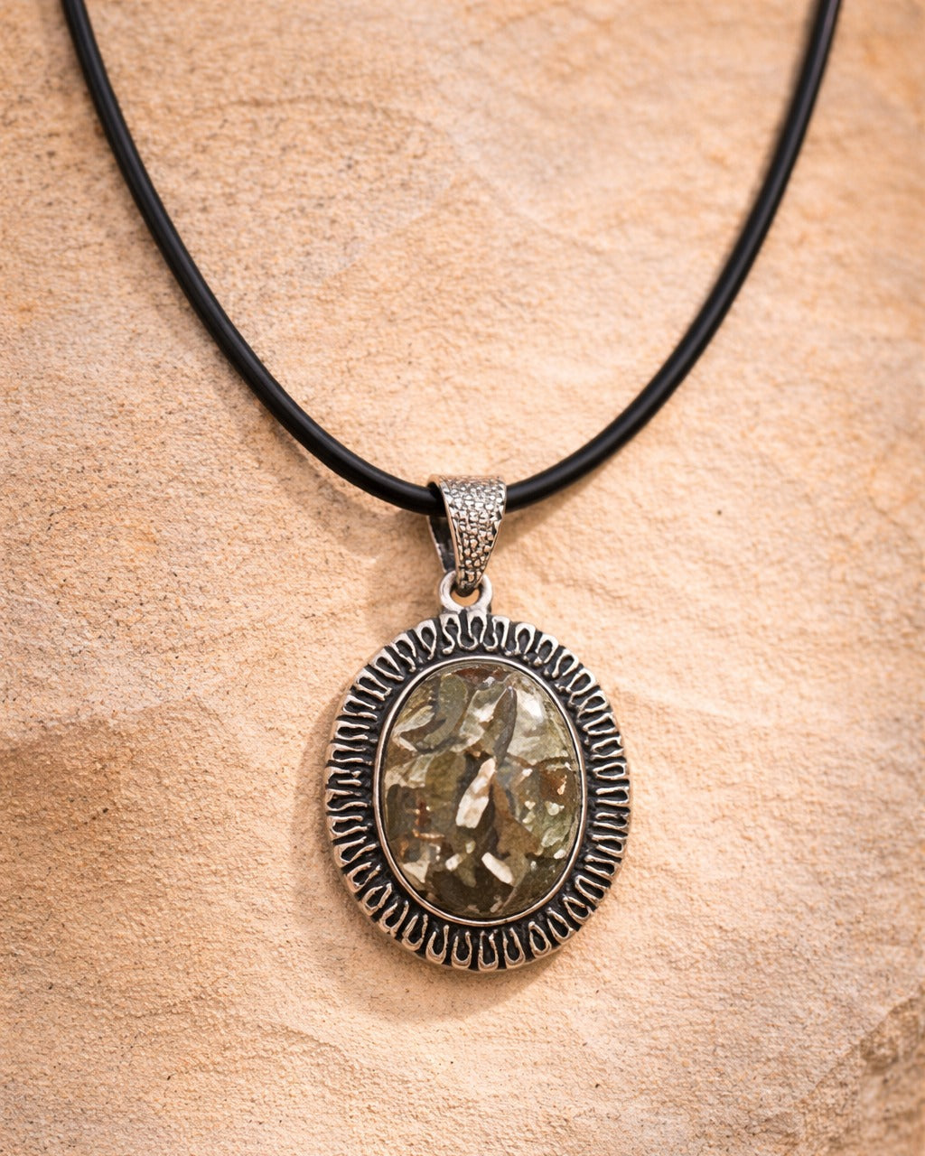 Silver pendant necklace on a black cord against a wooden background