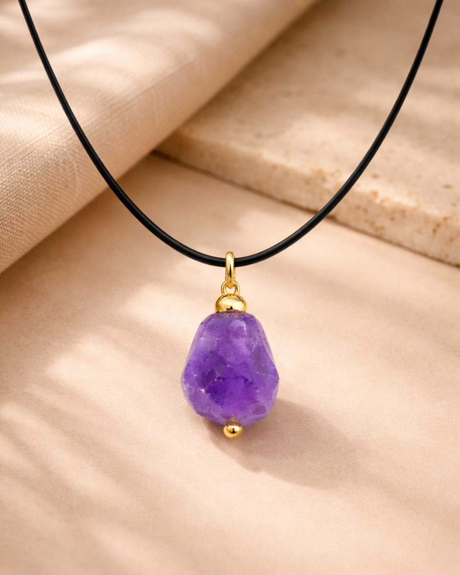 Raw amethyst wire wrapped pendant with black cord on beige background
