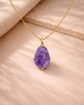 Raw amethyst wire wrapped pendant with gold chain on beige background