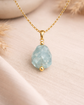 Raw aquamarine stone gold plated pendant on beige background