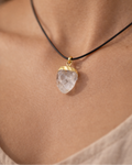 Necklace with a clear crystal pendant on a black cord, worn by a person.
