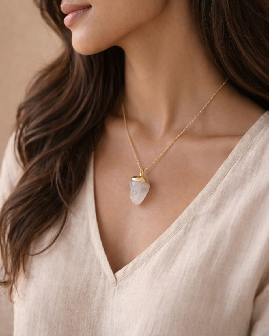 Woman wearing a gold necklace with a clear pendant against a neutral background