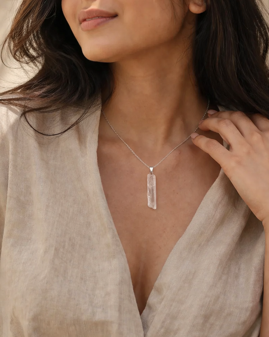 Woman wearing a beige garment and a necklace with a clear pendant against a neutral background