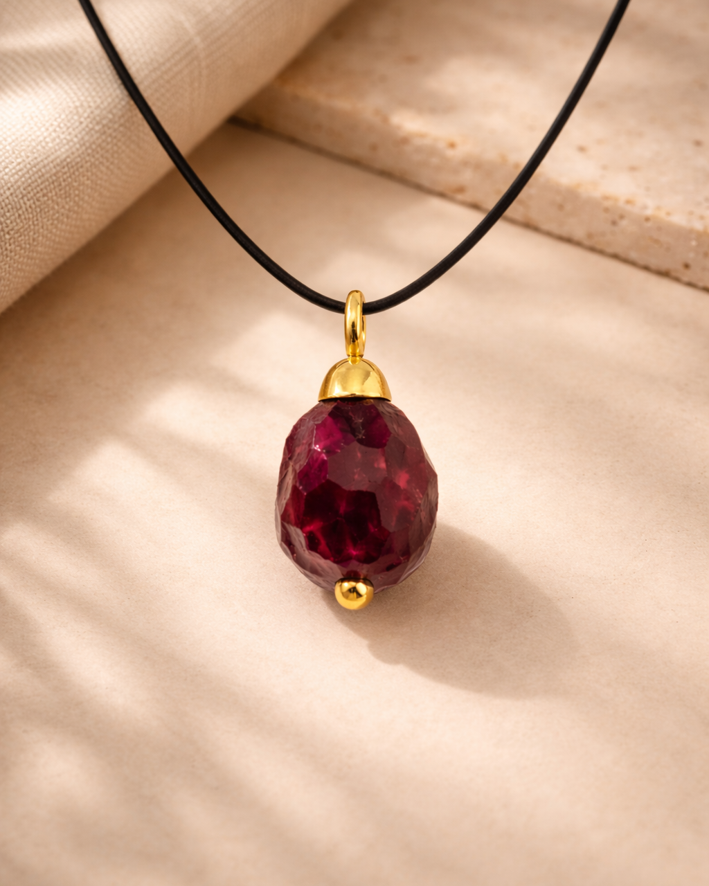 Raw drilled garnet necklace with black cord on beige background