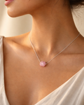 Woman wearing a necklace with a pink pendant against a neutral background
