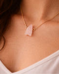 Necklace with a pink stone pendant on a person wearing a white top.