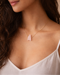 Woman wearing a delicate necklace with a pink pendant against a neutral background