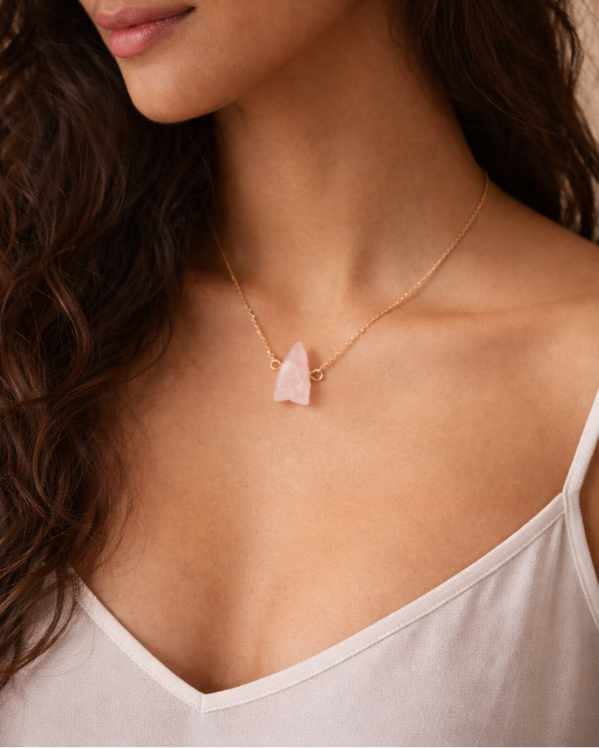 Woman wearing a delicate necklace with a pink pendant against a neutral background