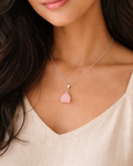 Woman wearing a necklace with a pink pendant against a neutral background