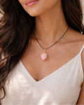 Woman wearing a necklace with a pink heart pendant against a neutral background