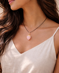Woman wearing a necklace with a pink pendant against a neutral background