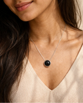Woman wearing a necklace with a black pendant against a neutral background
