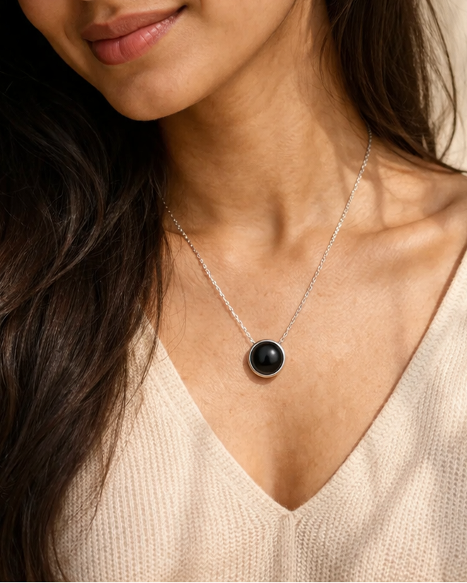 Woman wearing a necklace with a black pendant against a neutral background