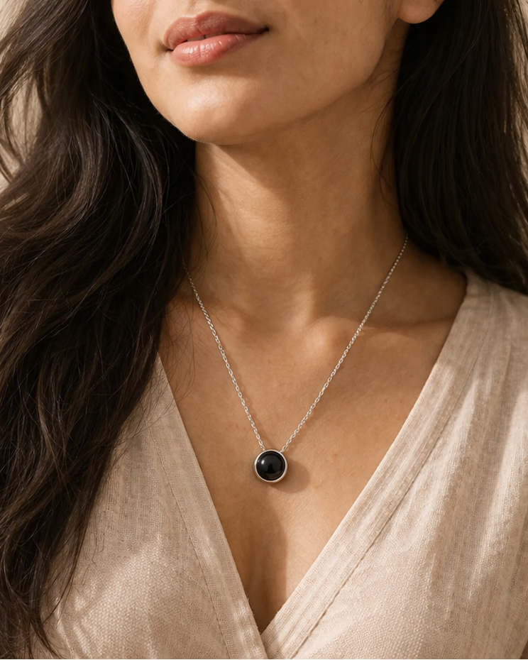 Woman wearing a necklace with a black pendant against a neutral background
