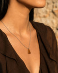 Necklace with a triangular Tiger Eye Stone  pendant worn by a person against a blurred natural background