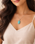 Woman wearing a necklace with a turquoise pendant against a neutral background