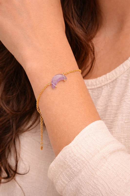 Person wearing a gold bracelet with a purple heart charm on a neutral background