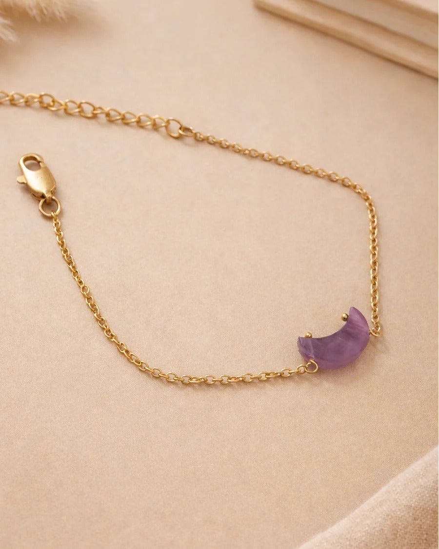 Gold bracelet with a purple crescent moon charm on a beige background