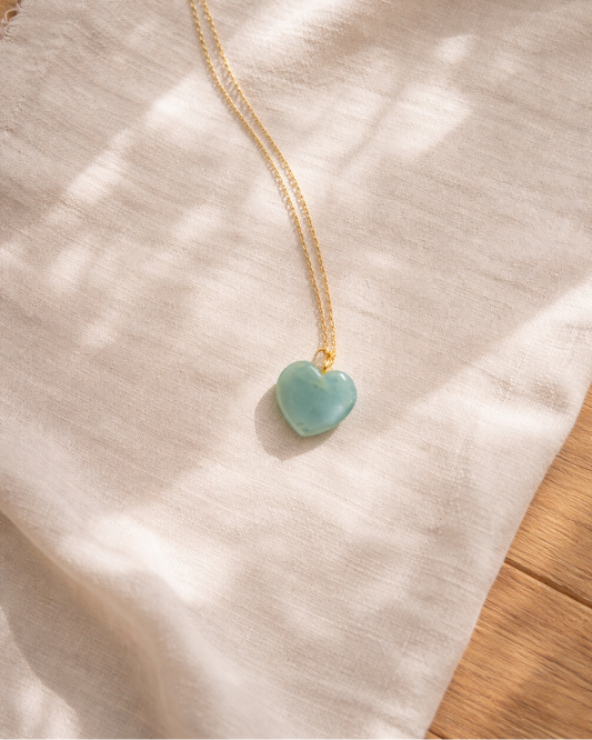 aquamarine heart pendant necklace on gold chain placed on beige surface showing soft ocean blue stone