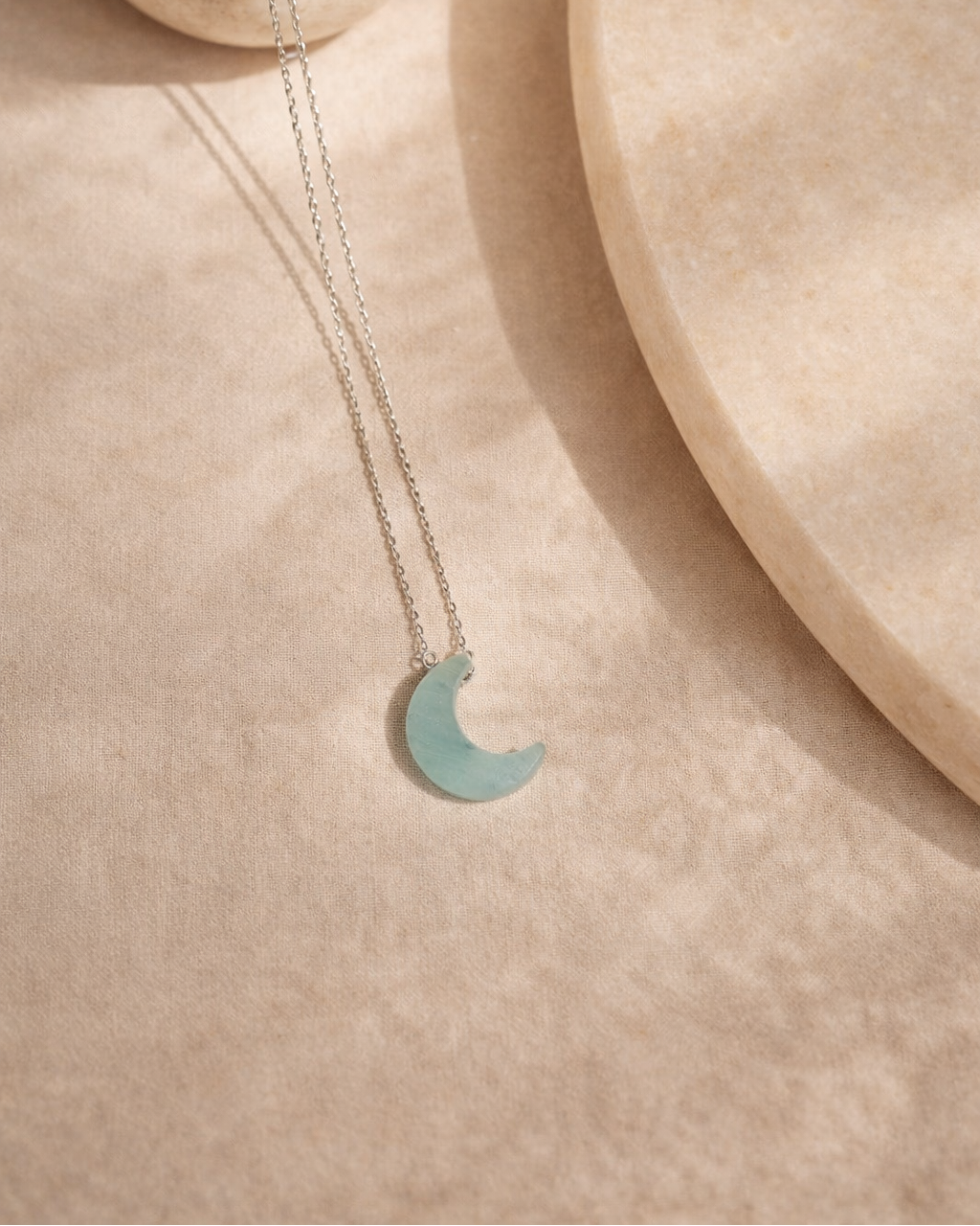 aquamarine moon pendant necklace on silver chain placed on beige surface showing soft ocean blue stone