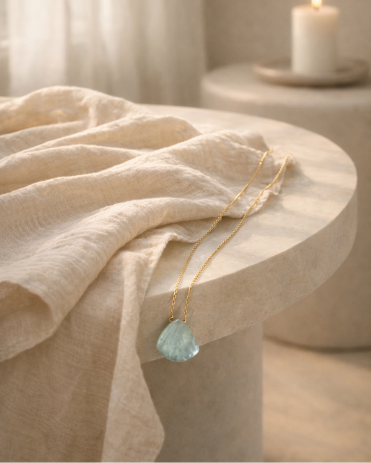 aquamarine pendant necklace on gold chain placed on beige surface showing soft ocean blue stone