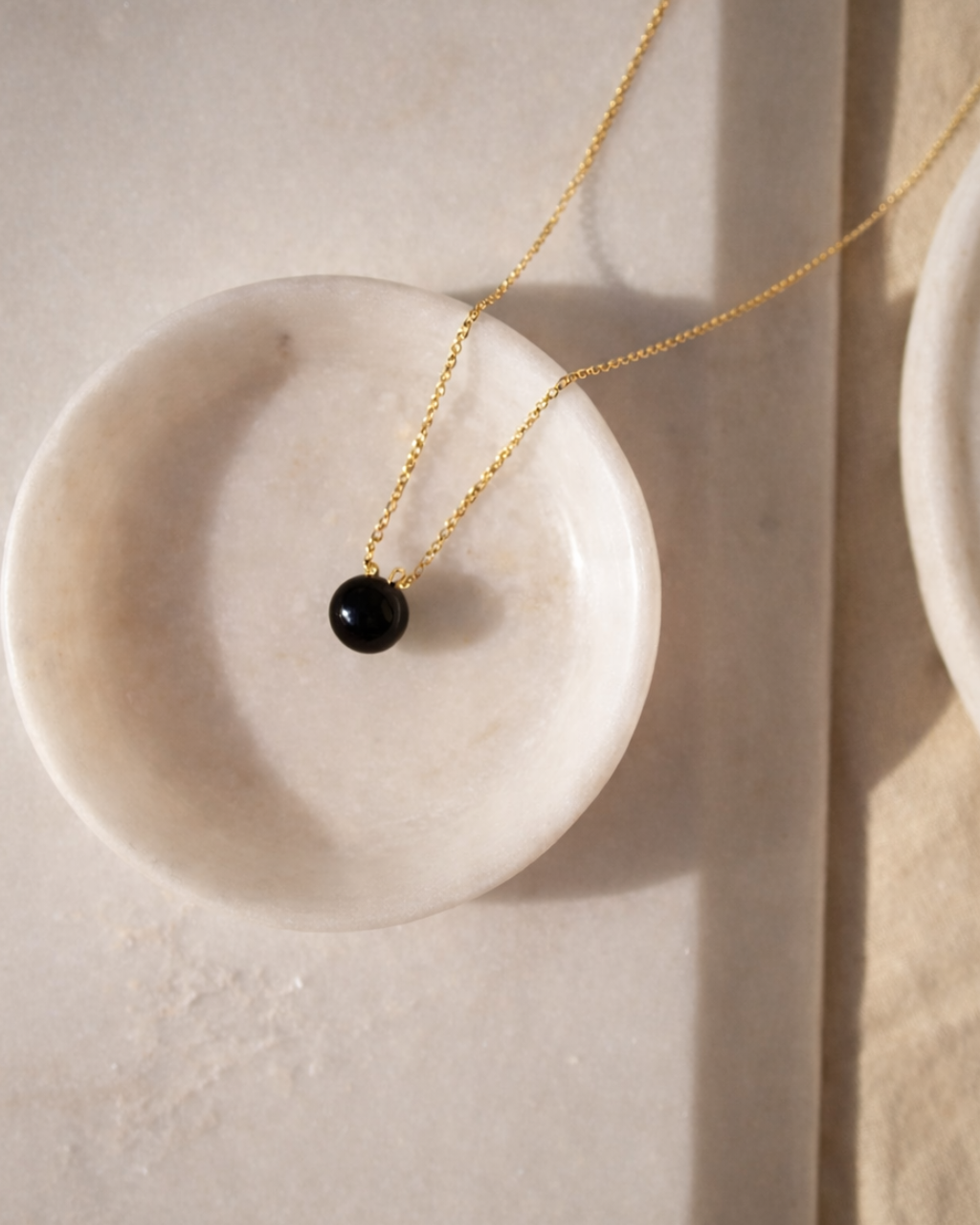 black onyx heart drop pendant necklace on gold chain placed on beige surface