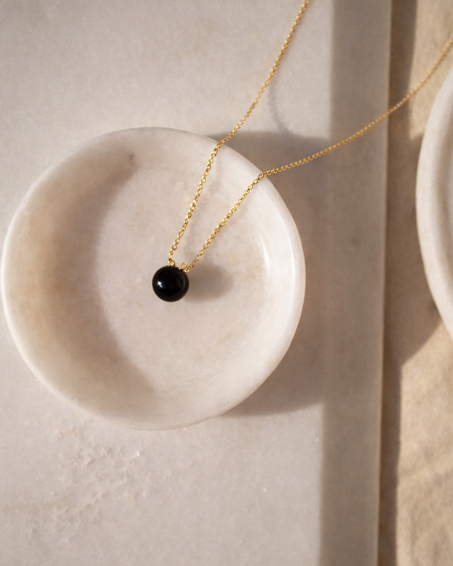black onyx heart drop pendant necklace on gold chain placed on beige surface