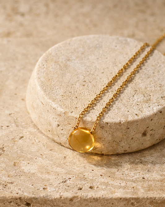 citrine heart shaped drop pendant necklace on gold chain placed on beige surface showing golden yellow stone