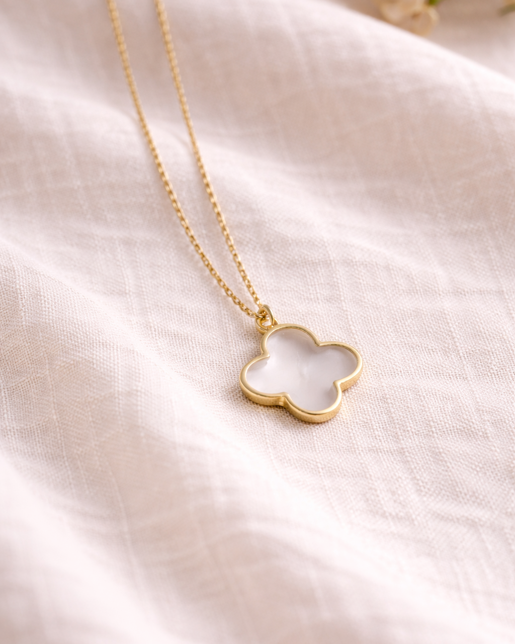Clear quartz clover pendant on gold chain placed on soft beige fabric, minimal elegant gemstone jewelry