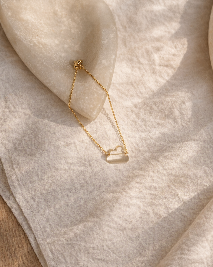 clear quartz cloud bracelet on gold chain placed on beige fabric showing transparent crystal stone