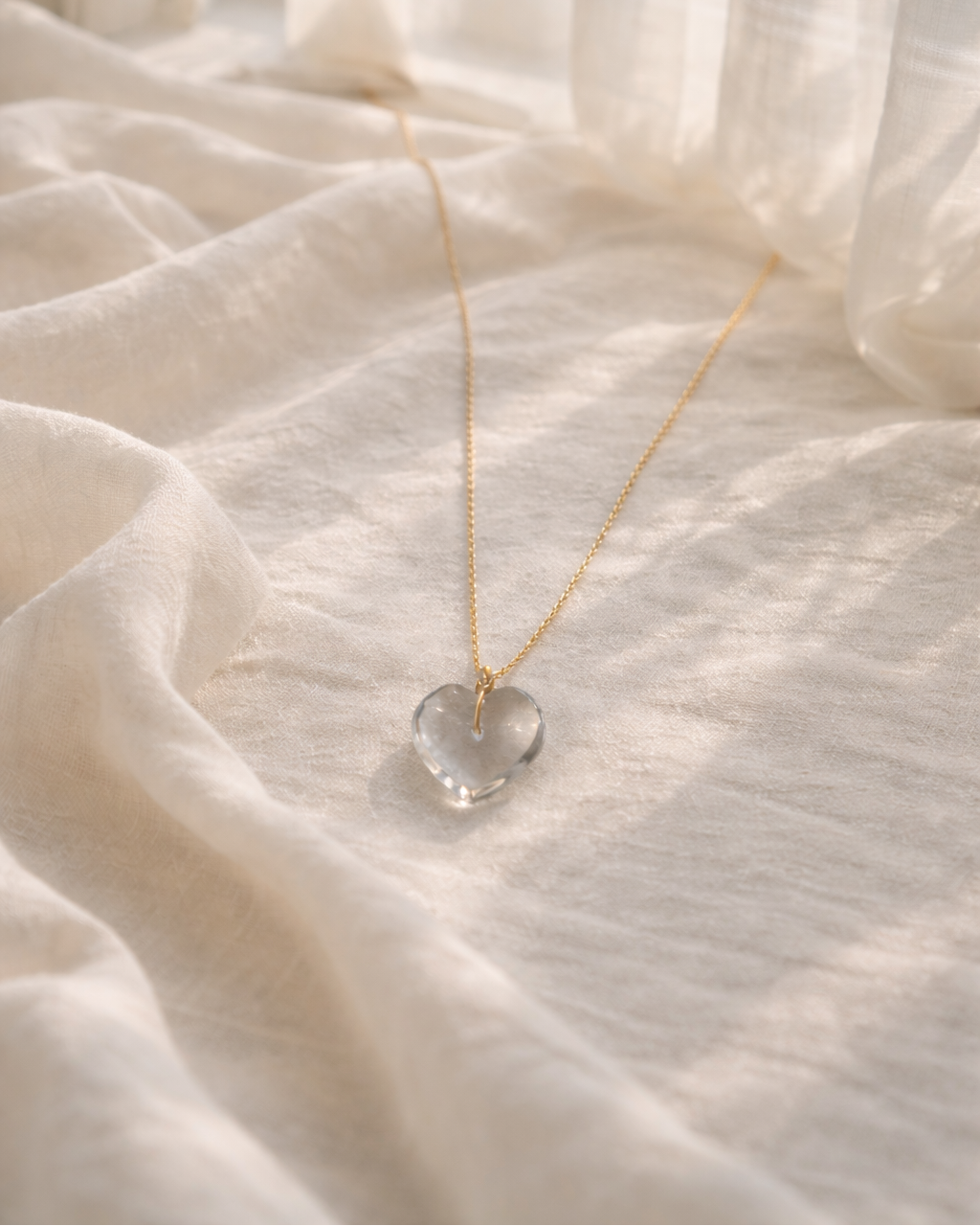 clear quartz heart pendant necklace on gold chain placed on beige fabric showing transparent natural stone