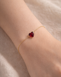 Delicate gold bracelet with red heart charm worn on wrist, showcasing elegant everyday jewelry style