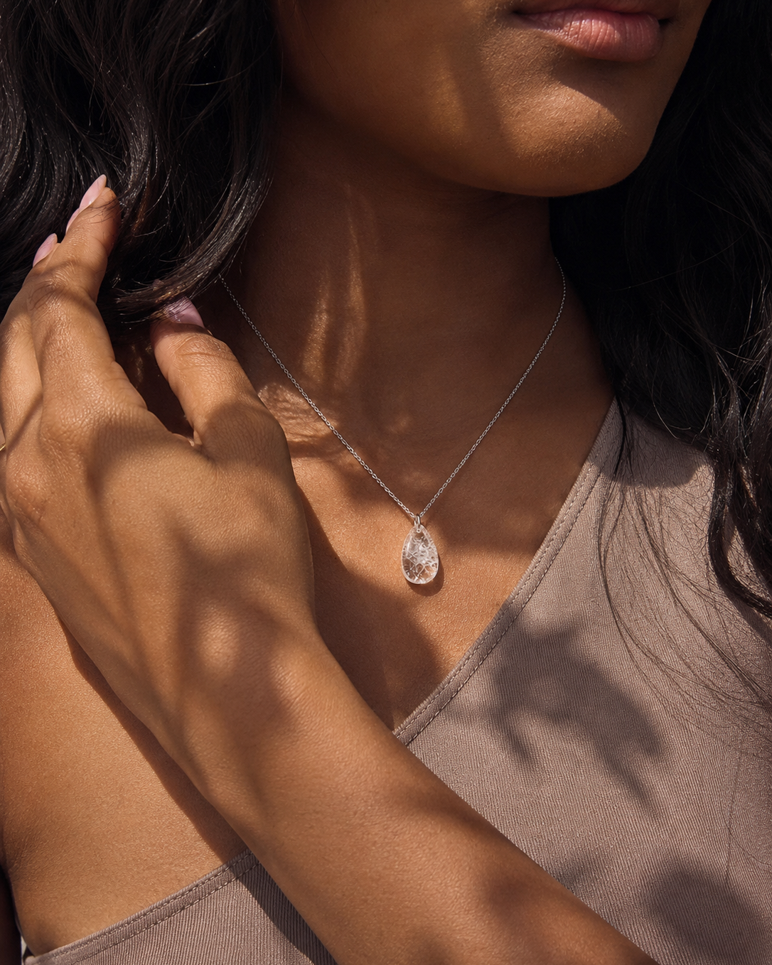 Woman wearing natural clear quartz teardrop pendant necklace in natural sunlight