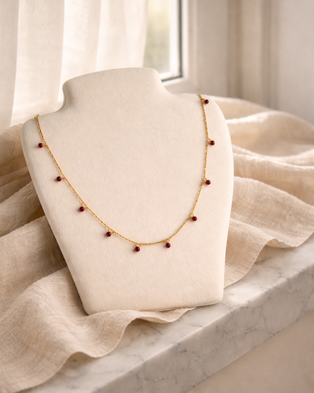 natural garnet bracelet on gold chain placed on beige fabric surface minimal jewelry