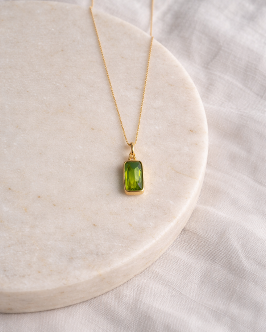peridot rectangle pendant necklace on gold chain placed on beige surface