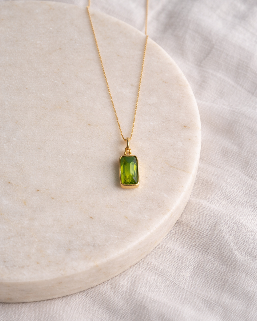 peridot rectangle pendant necklace on gold chain placed on beige surface