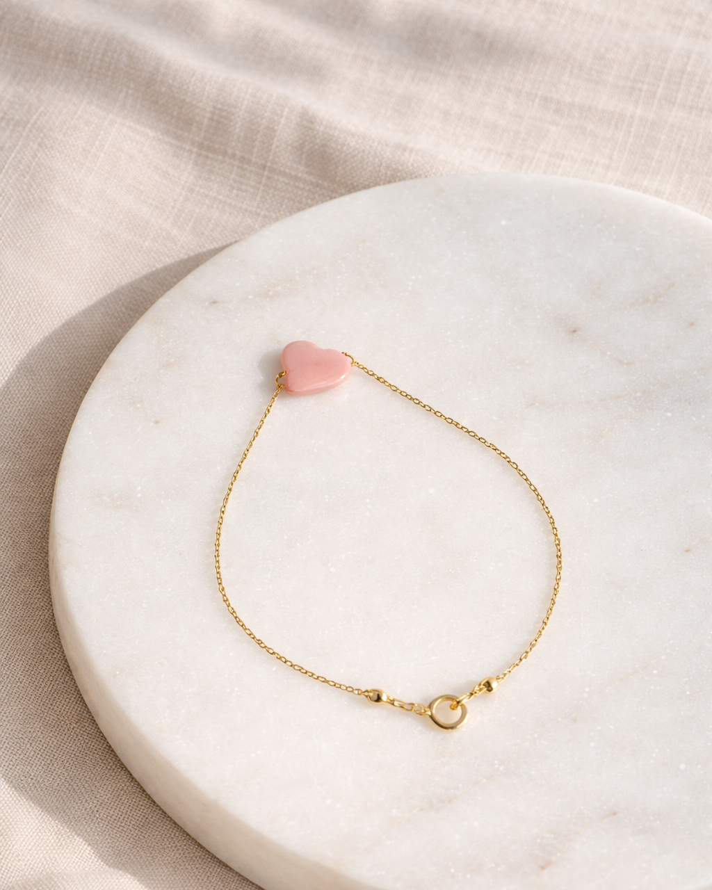 pink opal cloud bracelet on gold chain placed on beige surface minimal jewelry