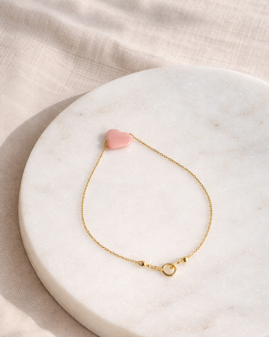 pink opal cloud bracelet on gold chain placed on beige surface minimal jewelry