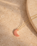 pink opal luna moon pendant necklace on gold chain placed on beige surface showing soft blush pink stone