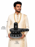 Hand-carved 0.8 ft Tripundra Shiva Lingam statue in polished black stone shown with an adult model for scale and measurements.